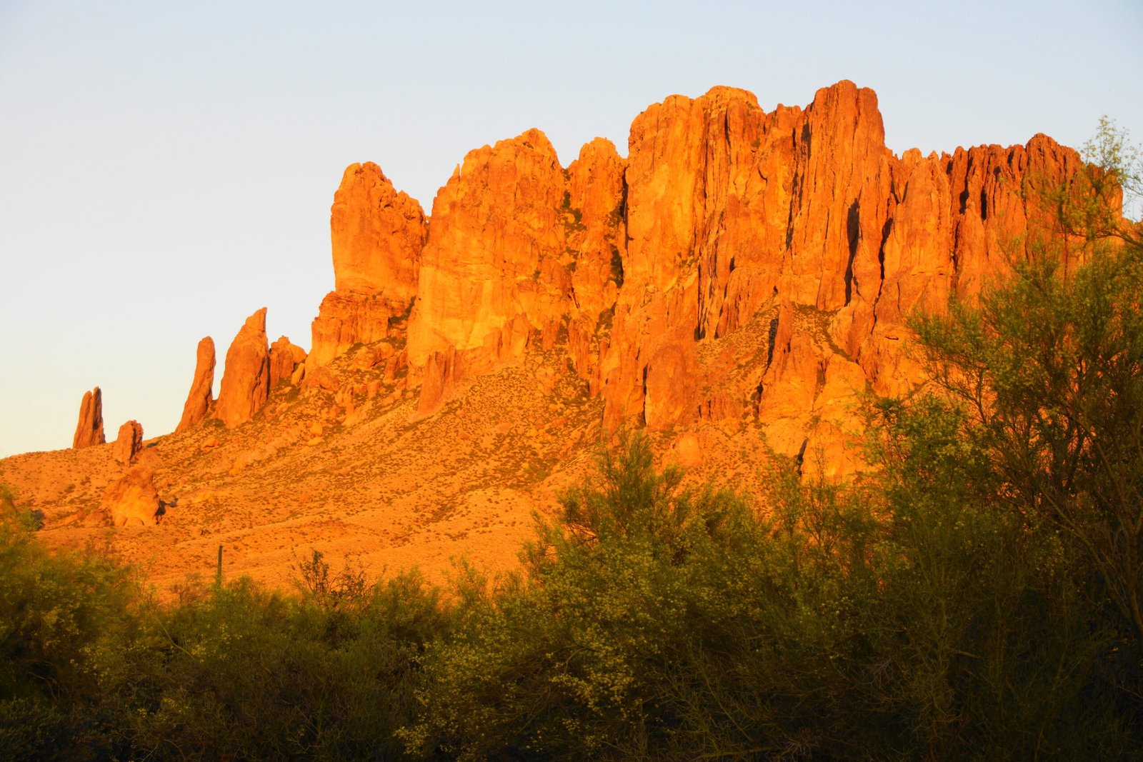Superstition Mountains glowing orange at sunset over desert brush